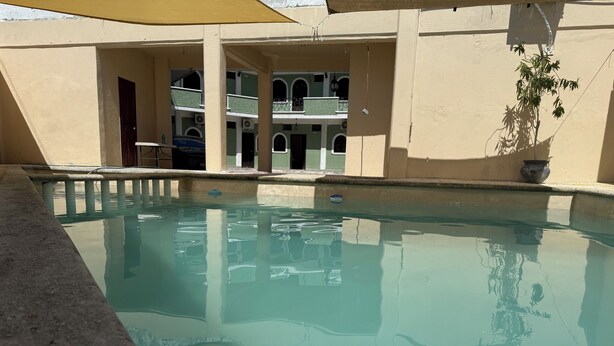 A swimming pool with clear water, surrounded by a building with multiple balconies and a shaded area. - Hotel Colonial (Escárcega)
