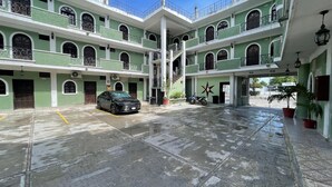 A multi-story building with a central staircase, a black car parked in the parking area, and potted plants on the ground floor. - Hotel Colonial (Escárcega)