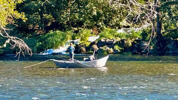 A boat on a river with a rocky shore and trees in the background.