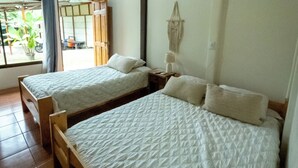 Dos camas individuales con cabeceros de madera y ropa de cama blanca en una habitación con techo de madera y un ventanal grande.
