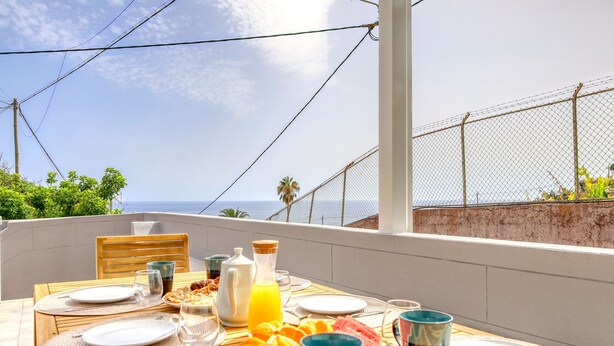 A breakfast table set on a balcony overlooking the sea, with plates, cutlery, and a variety of breakfast items. - Aunt Celeste's House I, a Home in Madeira (Ponta do Sol)
