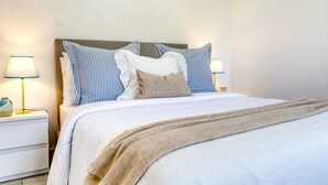 A neatly made bed with striped pillows and a beige throw blanket, flanked by two bedside lamps on white nightstands. - Aunt Celeste's House I, a Home in Madeira (Ponta do Sol)