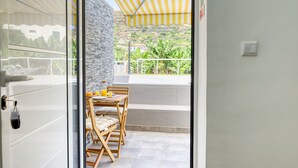 A balcony with a table and chairs, a yellow striped awning, and a view of greenery and buildings. - Aunt Celeste's House III, a Home in Madeira (Ponta do Sol)
