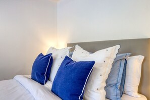 Ein Bett mit weißer und blauer Bettwäsche, einem grauen Kopfteil und einer Wandleuchte.