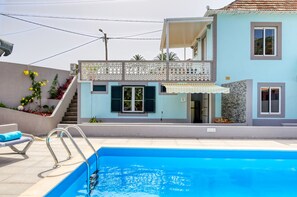 Ein modernes, zweistöckiges Haus mit Swimmingpool, einem Balkon mit weißem Gitter und einer kleinen Sitzgruppe im Freien.