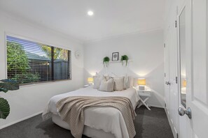 A bedroom with a bed, bedside tables, a window with blinds, and a door.