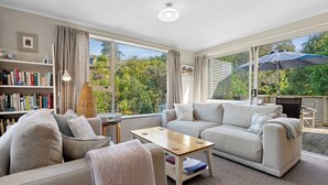 A spacious living room with a large window, a bookshelf, a sofa, a coffee table, and a view of the outdoors.