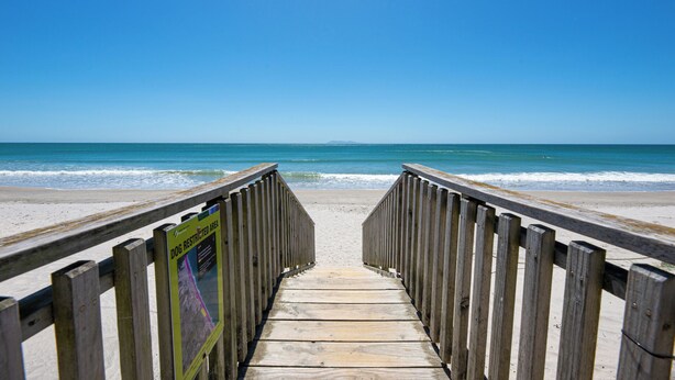 A wooden boardwalk leading to a beach with a clear blue sky.