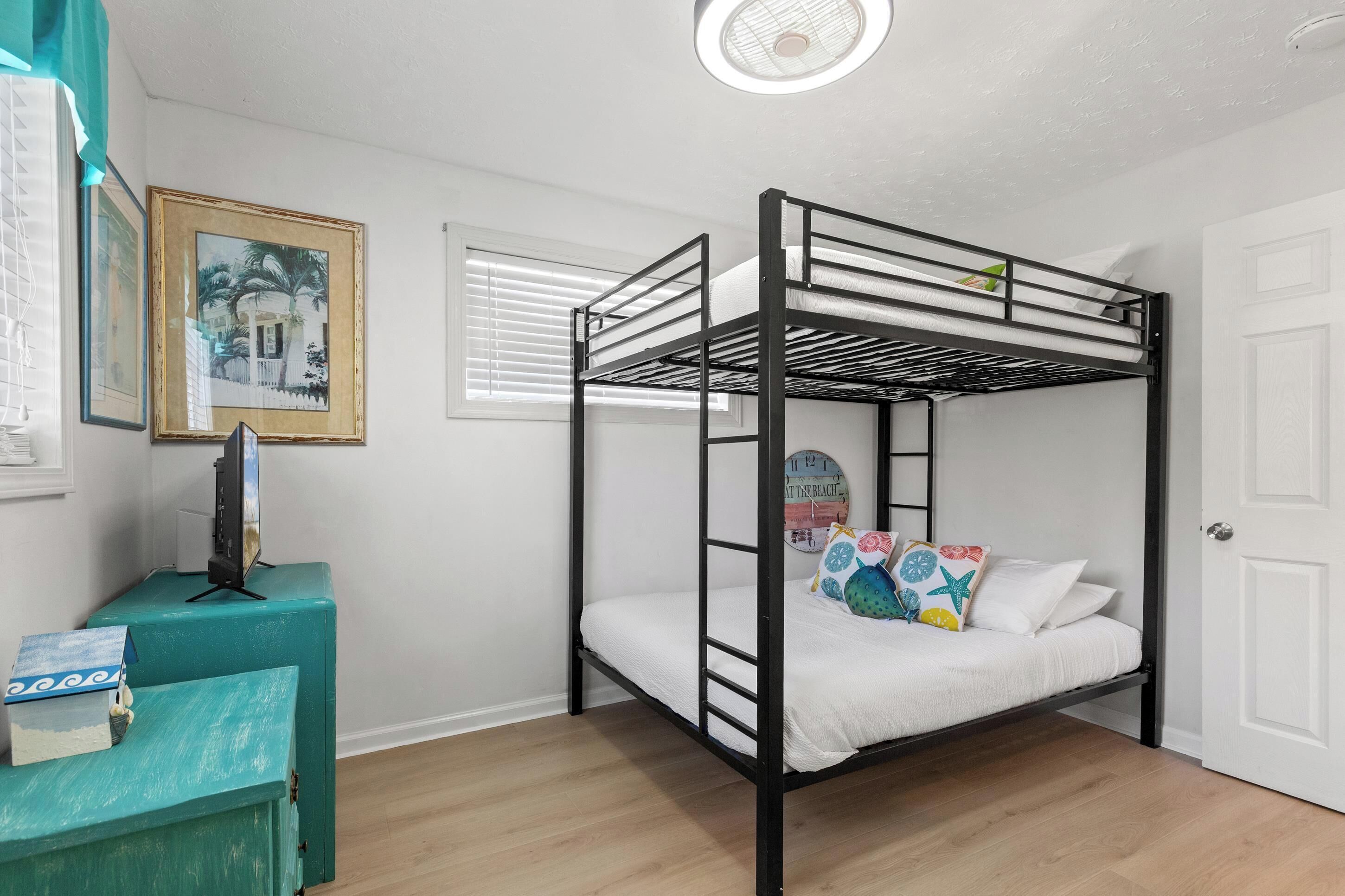 A bunk bed with a white mattress, a small desk with a television, and a framed picture on the wall.