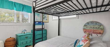 A bunk bed with a metal frame, a teal dresser, a woven basket, and a wall clock.