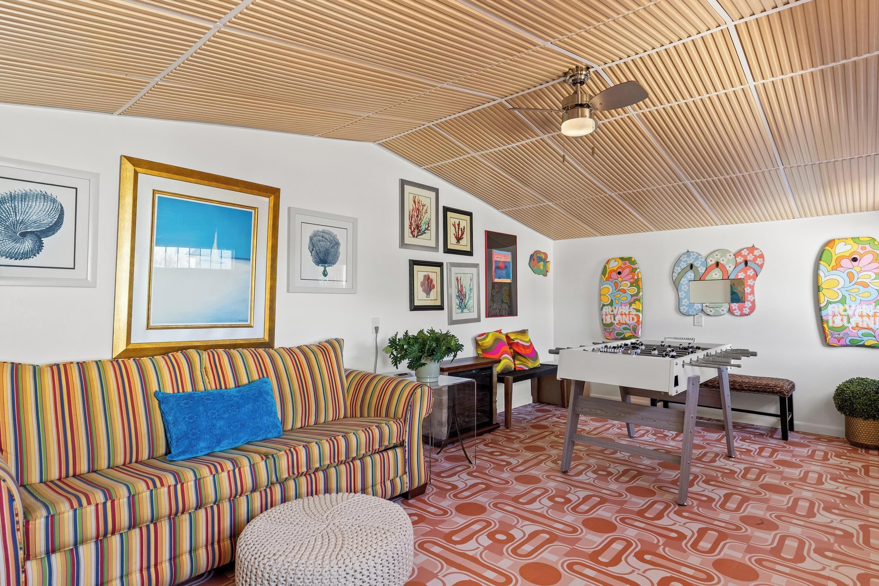 A room with a striped sofa, a foosball table, and various framed artworks on the walls.