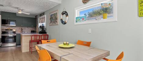 Une cuisine moderne avec des meubles de couleur sombre, un îlot central en bois et un coin repas avec des chaises orange et une table en bois.