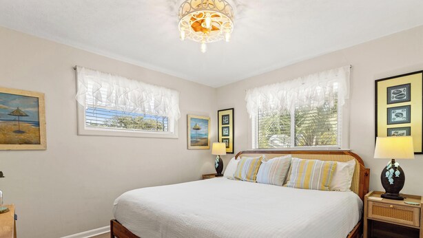 Une chambre à coucher avec un grand lit, deux tables de chevet, un lustre et des tableaux encadrés accrochés aux murs.