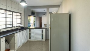 Una cocina compacta con refrigerador integrado, una ventana con persianas y una lámpara colgante.