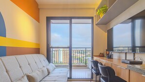 A modern apartment with a sofa, a dining area, and a balcony with a city view. - Nex One Nhambiquaras (São Paulo)