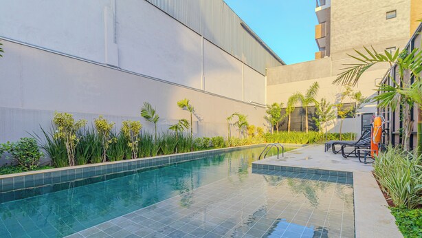 A swimming pool with tiled edges, surrounded by greenery and a building facade. - Nex One Nhambiquaras (São Paulo)