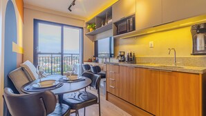 A modern kitchen with a dining area, featuring a large window with a view, wooden cabinets, and a countertop with a coffee machine. - Nex One Nhambiquaras (São Paulo)