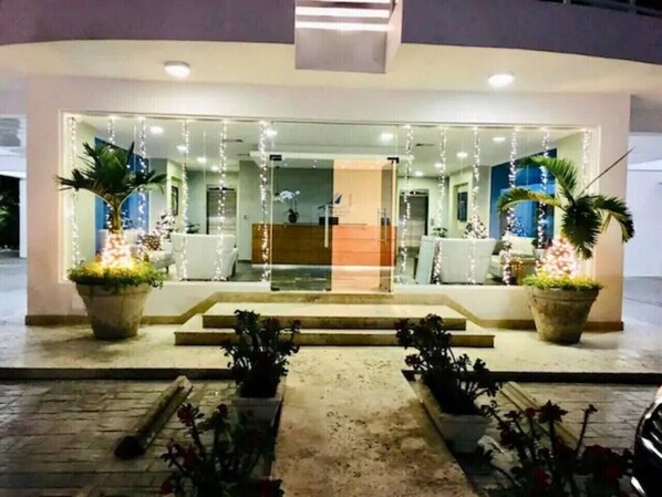 A hotel entrance with a glass facade, steps leading up to the door, and potted plants on either side.