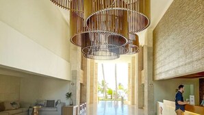 Un hall d’entrée spacieux, agrémenté d’un lustre moderne, d’un comptoir de réception et offrant une vue sur des palmiers.