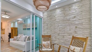 Un salon moderne doté d’une cloison en verre, d’un canapé blanc, de deux fauteuils à bascule en bois et d’un mur en pierre à texture.
