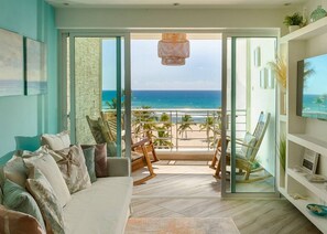 Een woonkamer met een grote glazen deur die leidt naar een balkon met uitzicht op de oceaan.