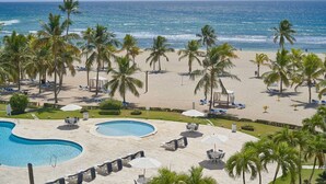 Un complexe hôtelier de bord de mer doté d’une piscine, de palmiers et de chaises longues.