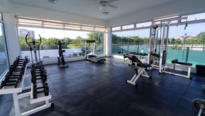 A spacious gym with various exercise equipment, large windows, and a ceiling fan.
