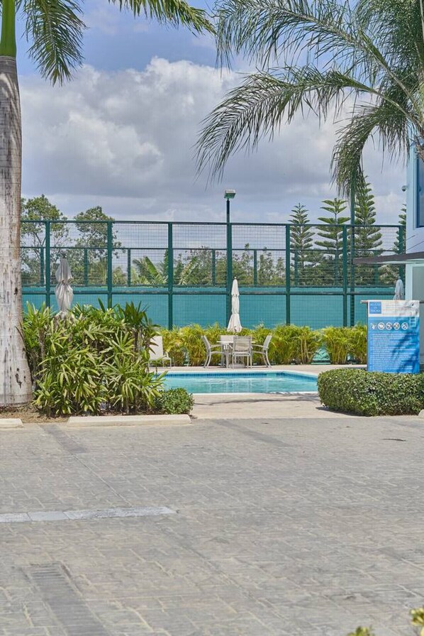 A pool area with a fenced patio, seating, and palm trees.