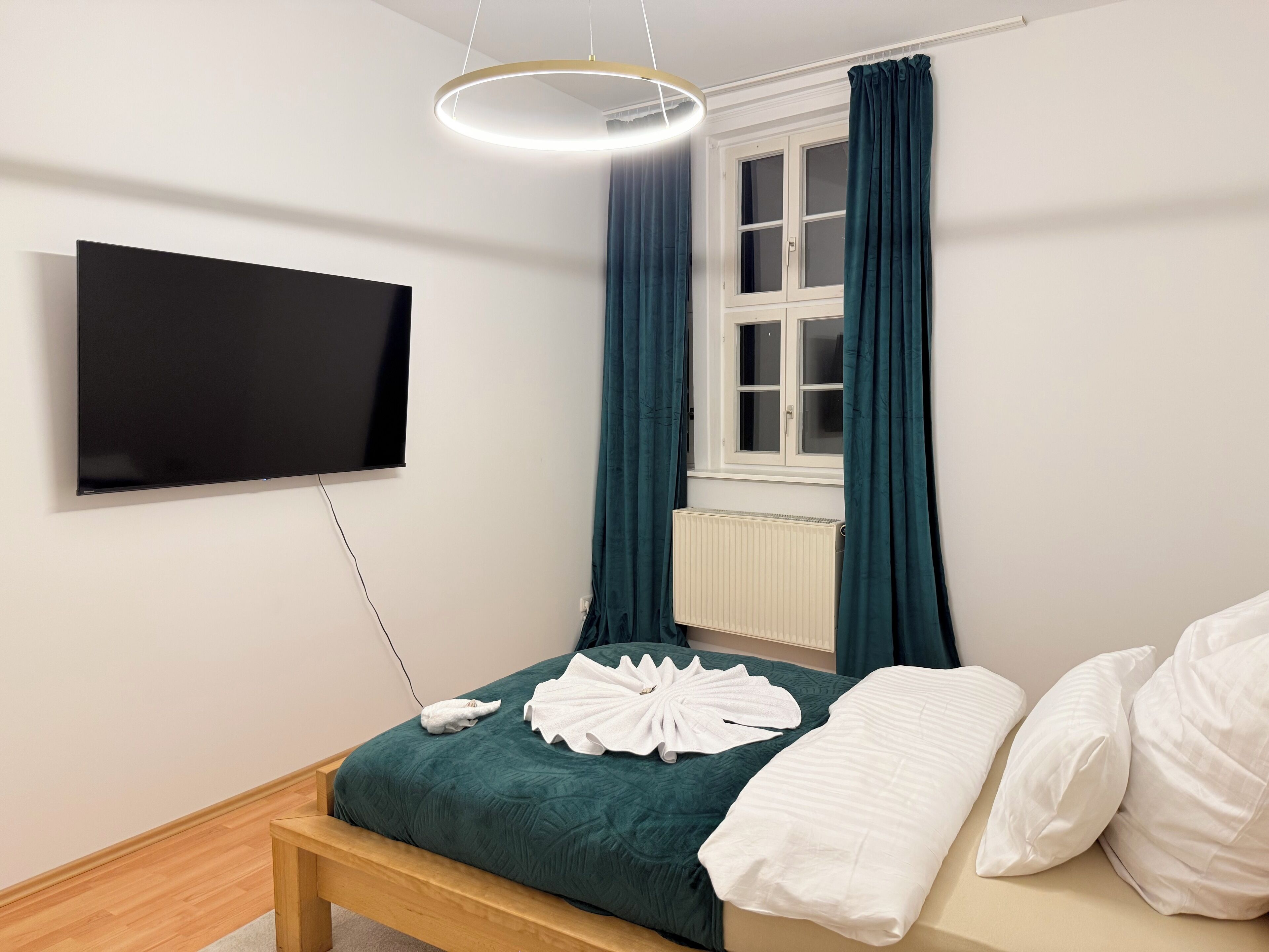 Ein modernes Schlafzimmer mit Bett, Wandfernseher und einem Fenster mit Vorhängen.