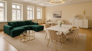 Un salón amplio con un sofá seccional verde, una mesa de centro redonda y una zona de comedor con mesa y sillas blancas.