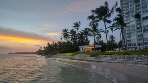 Een hotel aan het strand met een zwembad, palmbomen en uitzicht op de zonsondergang.