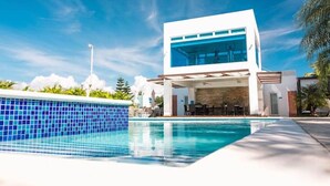 Ein modernes, zweistöckiges Gebäude mit einem großen Glasfenster, einem Swimmingpool und Außenplätzen.