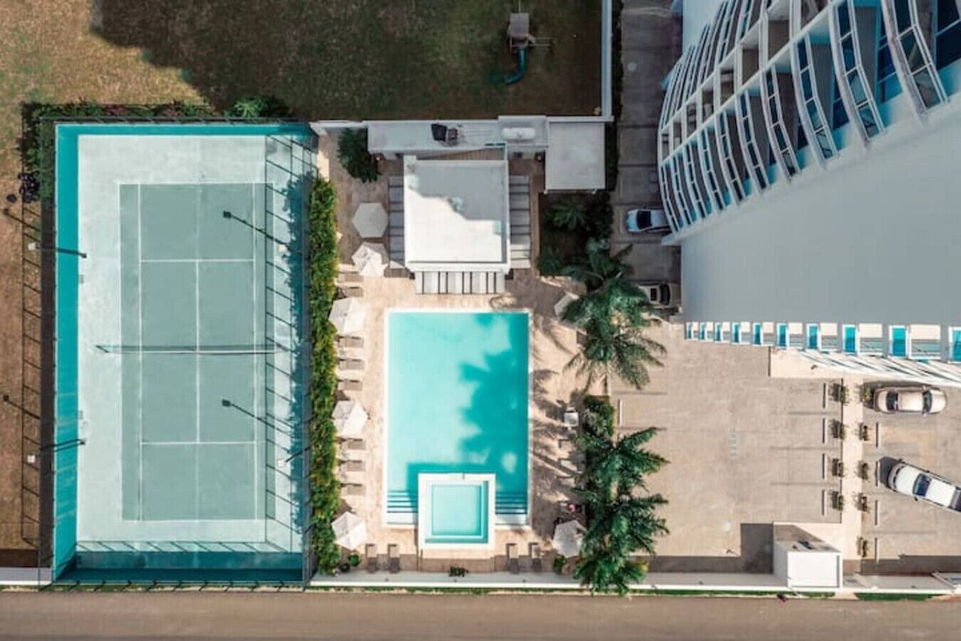 Vista aérea de un hotel con piscina, cancha de tenis y zona de estacionamiento.