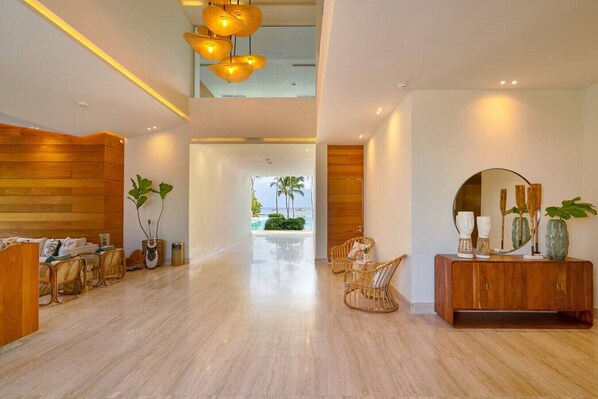 A spacious lobby with a wooden reception desk, wicker furniture, and a view of the pool and palm trees.