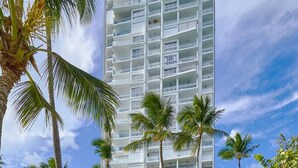 A high-rise hotel with a pool area, palm trees, and lounge chairs.
