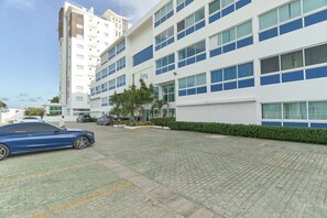 A modern building with multiple floors, large windows, and a parking area with cars.