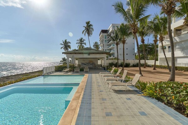 An infinity pool with a view of the ocean, lounge chairs, and palm trees.
