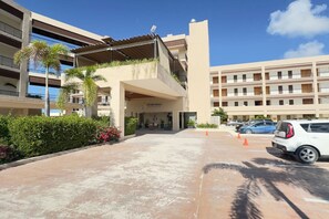 A hotel entrance with a covered walkway, a reception desk, and a parking area with cars.