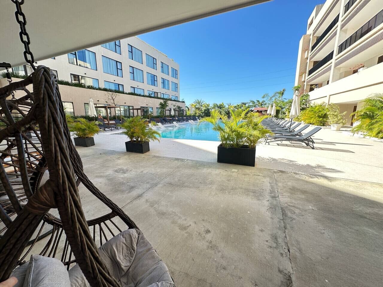 Un área junto a la piscina con sillones, piso de concreto y un edificio al fondo.