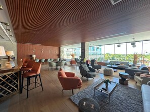 A spacious lounge area with multiple seating options, a bar area, and large windows offering a view of the outdoors.