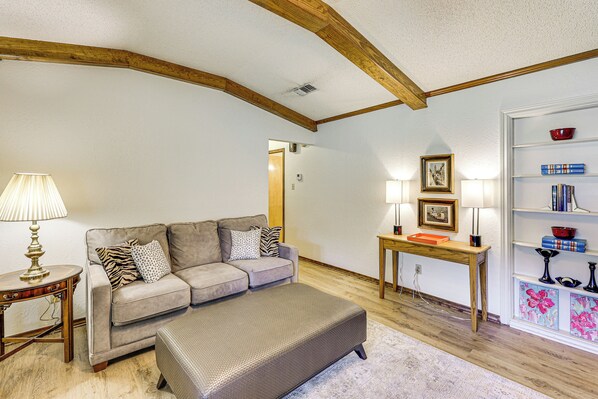 A living room with a sofa, ottoman, wooden table, and bookshelf.