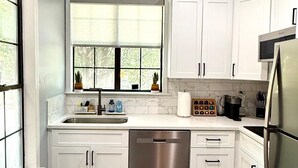 A modern kitchen with white cabinets, a stainless steel dishwasher, a microwave, and a refrigerator. - Stylish Midtown Atlanta Studio •Walk to Piedmont Park+ Free Covered Parking (Atlanta)