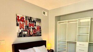 A neatly made bed with white linens and a folded towel, a wall-mounted poster of New York, and a walk-in closet with white shelving. - Stylish Midtown Atlanta Studio •Walk to Piedmont Park+ Free Covered Parking (Atlanta)