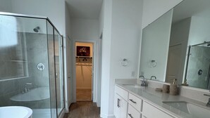 Et moderne badeværelse med brusekabine i glas, et stort spejl og trægulv.