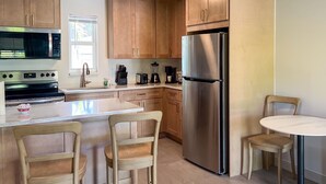 Une cuisine moderne avec des meubles en bois, des appareils en acier inoxydable, un îlot central doté de chaises et une petite table à manger.