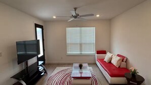 A living room with a flat-screen TV, a ceiling fan, a sofa, a coffee table, and a window with blinds.
