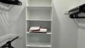 A walk-in closet with white shelving units and black hangers.