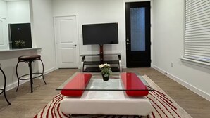 A modern living room with a glass coffee table, a red and white striped rug, a white sofa, a black TV on a stand, and a door with frosted glass.