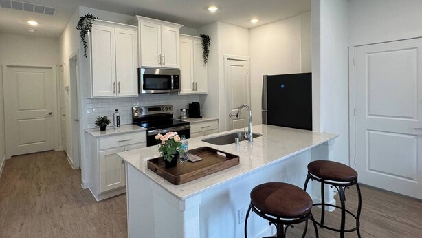 A modern kitchen with white cabinetry, stainless steel appliances, a central island with stools, and a black refrigerator.