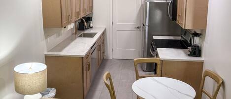 A compact kitchen with wooden cabinets, a white door, a refrigerator, a stove, and a small dining table with chairs.